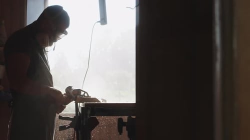 A Man in a Respirator Goggles Polishes a Wood Board with Grinder