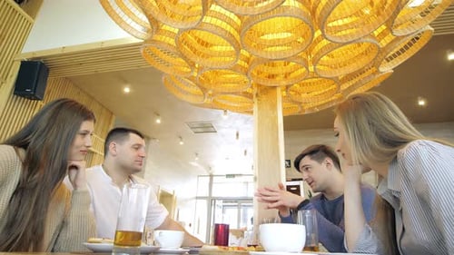 A Happy Group of Friends are Sitting at a Table in a Cozy Restaurant Laughing and Having Fun