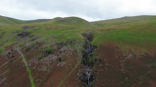 Slow zoom into waterfall on bleak empty hillside