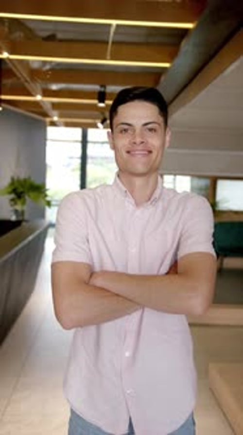 Vertical video: Smiling man standing with arms crossed in modern office hallway