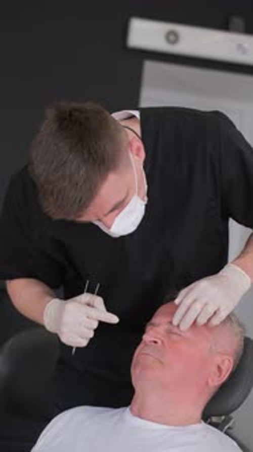 A Plastic Surgeon in a Copper Room Examines an Elderly Man's Face Vertical Video