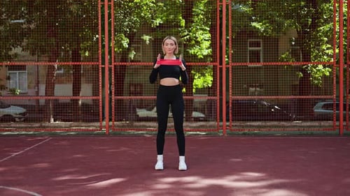 Woman Exercises With Resistance Band Outdoors on Court