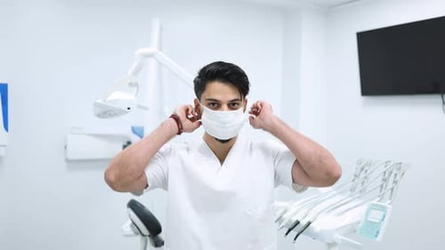 Portrait of male dentist putting on a surgical mask looking into the camera.
