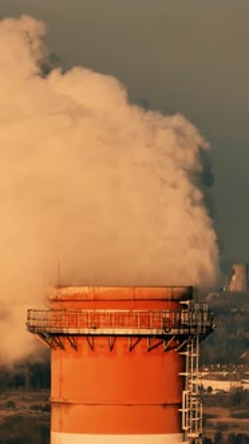 Smoke billowing from industrial smokestack in city during sunset