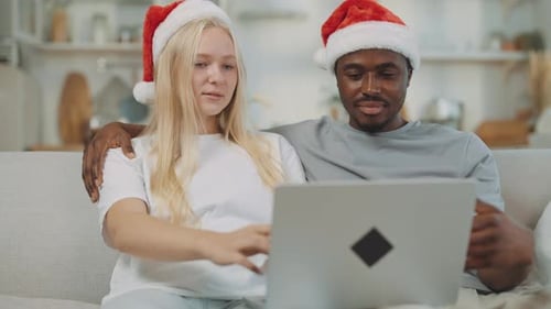 Couple wearing Santa hats using a laptop indoors