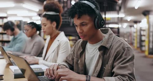 Man, student and headphones with laptop in library for typing assignment essay