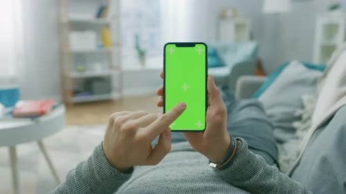 Man at Home Lying on a Couch using Smartphone with Green Mock-up Screen, Doing Swiping, Scrolling G