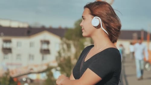 A Young Girl in White Headphones with Pleasure Listens to Music on a Warm Summer Evening