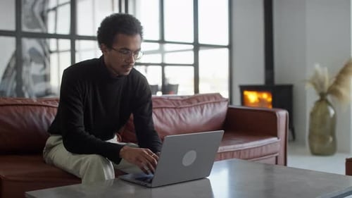 Young Man Working on Laptop in Cozy Modern Living Room with Fireplace