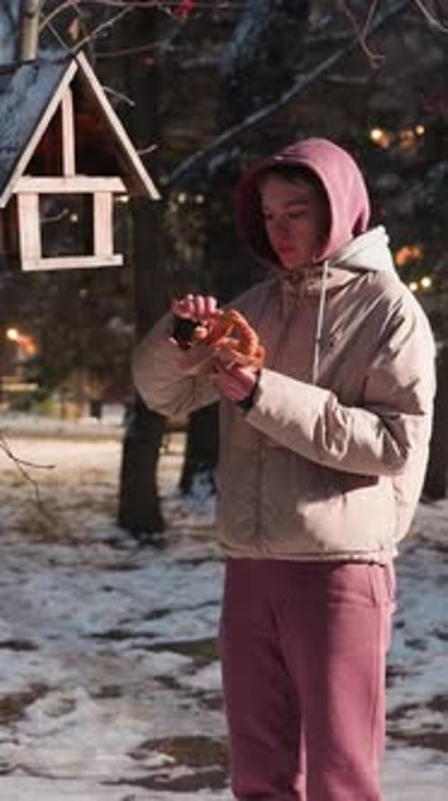Young Woman Feeding Birds in Winter Park with Snowy Ground and Park Lights