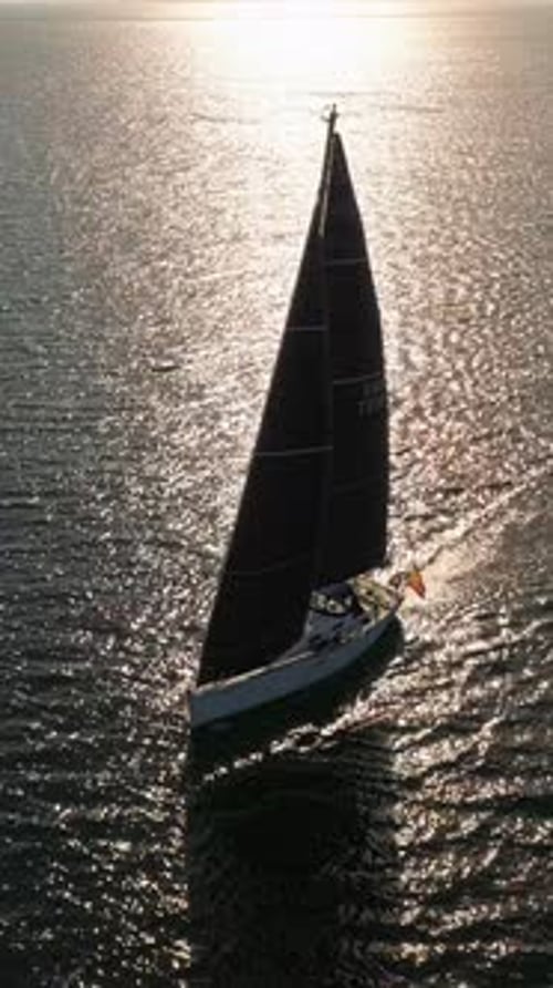 Vue aérienne d'ensemble d'un yacht blanc avec des voiles dans les rayons du soleil couchant, éblouissement du