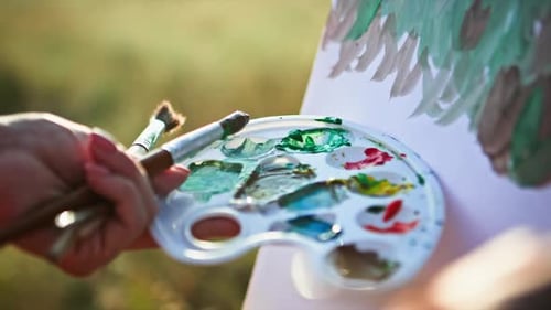 Creative Young Woman Using Paints and Brushes Mixes Paints in a Palette and Draws Picture on Hot