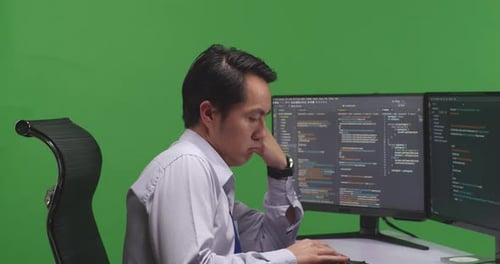 Close Up Of Developer Boring While Write Code With Multiple Computer Screens In Green Screen Studio