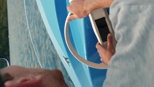 Male hands turning wheel on tourist electric boat on lake. Vertical video
