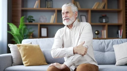 Senior Man Massaging Sore Arm While Sitting on Couch