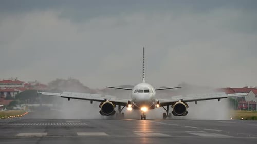 Airplane Landing on Runway with Water Spray and Cloudy Sky Creating Dramatic Atmosphere