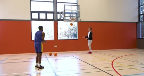 Practicing basketball, coach and player focusing on dribbling skills in gym