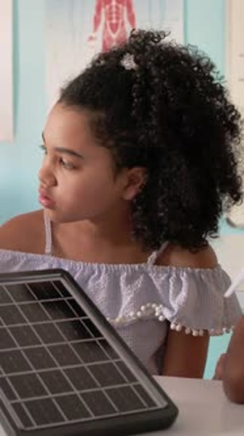 Vertical video: Turning kid in blue top watching teacher entering right in class showing solar wind