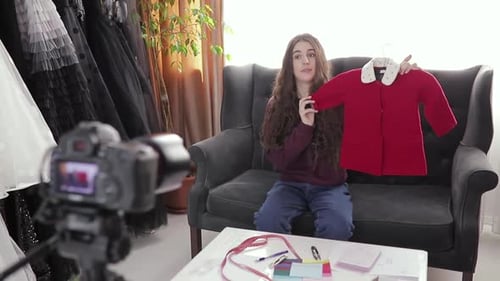Vídeo de reseña de ropa de mujer joven sonriente sentada en el sofá de su casa
