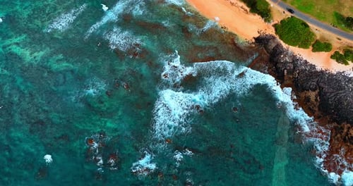 Foamy waves roll to the sandy beach and rocks at the coast.