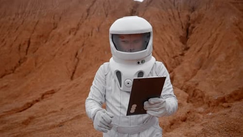 Astronaut Special Suit and Helmet Walks with a Tablet on the Surface of Mars