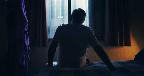 Man Sitting on Bed and Looking out Window