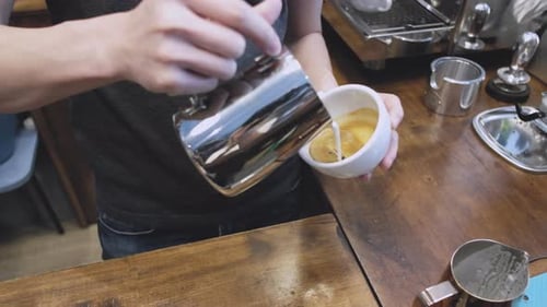 Close up of Barista man hands pouring warm milk in coffee cup for making latte art at coffee shop.