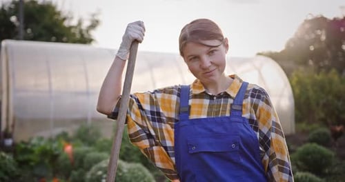 Confident Young Gardener with Shovel in Backyard Greenhouse Garden