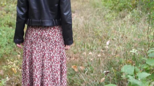 Brunette girl in the autumn forest walks down a path and grabs her hair