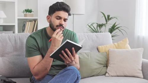 Young Man Writing in Notepad on Sofa