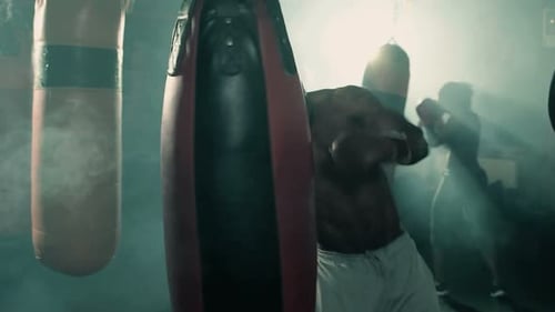 Shirtless man boxing with punching bag in smoky gym