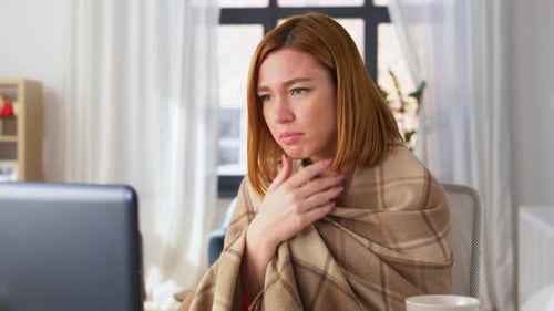 Sick Woman Video Conferencing with Laptop, Wrapped in Blanket
