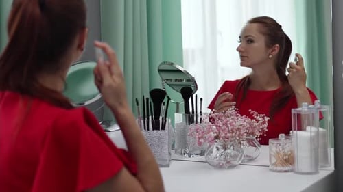 Woman Applying Makeup in Front of a Mirror