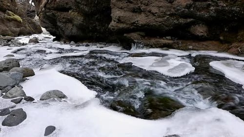 Une rivière au courant rapide qui traverse des rochers recouverts de neige et de glace au début du printemps. Islande.