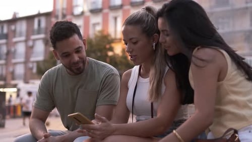 Happy Friends Using Smartphone Together in City During Sunset