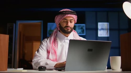 Man Works On Laptop At Office Desk At Night