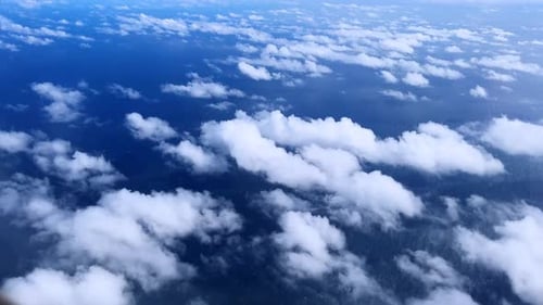 White clouds float over a vast blue ocean seen from above during a peaceful aerial flight