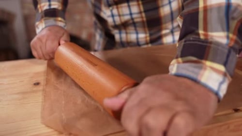 Person Rolling Dough on Wooden Table Surface
