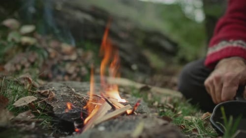 Hands of Man Tending Campfire and Using Metal Pan to Prepare Meal in Forest