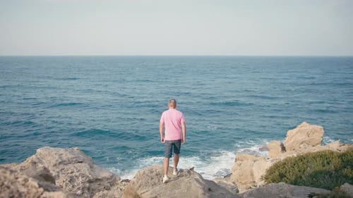 Middle Aged Man Standing on Rocky Shore Facing the Sea