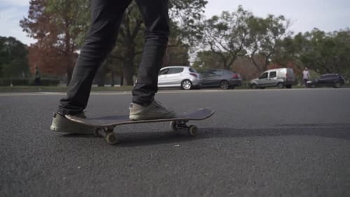 the legs and board of a skateboarder who skates past on an asphalt road in slow motion