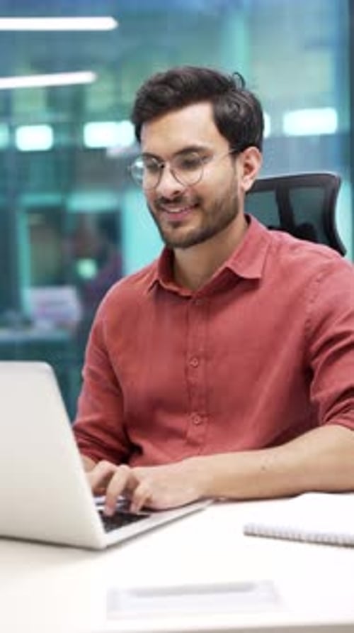 Smiling male professional at workplace typing on laptop in modern office desk. Businessman engaged