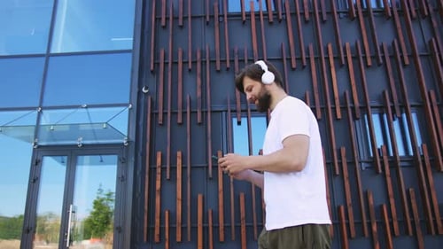 Handsome Young Caucasian Man in Sportswear and Headphones Walking the Street Listening to Music and