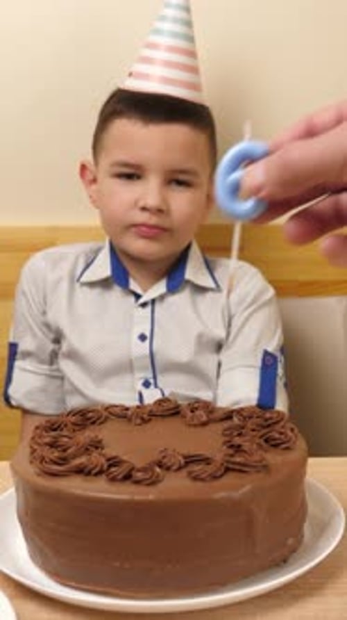43. A boy is sitting in front of a table with a birthday cake, into which a candle in the form of th