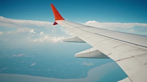 Tragfläche eines über Meer und Insel fliegenden Flugzeugs vom Fenster auf Wolken in blauem bewölktem Himmel Flugzeugflügel