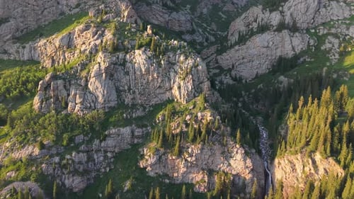 Sunlight Illuminating Rocky Mountain with Coniferous Forest and Waterfall