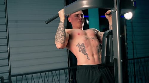 in the Gym Young Handsome Guy with Tattoos is Doing Pullups on the Horizontal Bar Shaking His Back