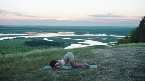 Yoga auf dem Hügel: Eine Frau, die bei frühem Sonnenuntergang auf einer Yogamatte trainiert und den Rücken beugt