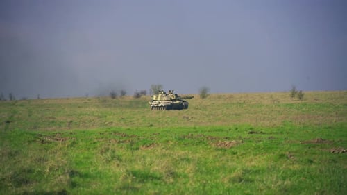 Military tank driving across open grassland during live training exercise in UK