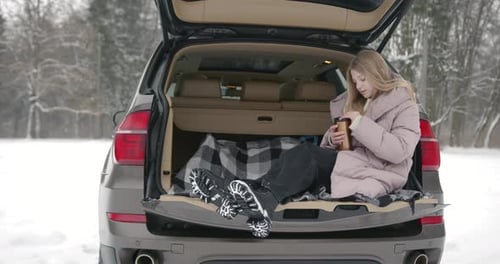Young Adult Relaxing in Car Trunk in Snowy Woods
